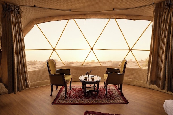 Una carpa con un diseño geométrico en la ventana, dos sillas, una mesita y un tapete rojo estampado.