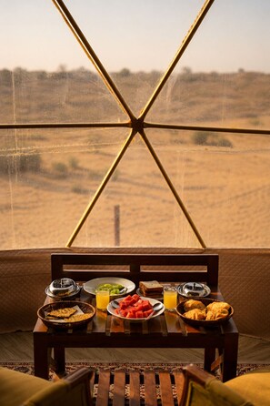 Una mesa de comedor con comida y bebidas, frente a una ventana con vistas a un paisaje desértico.