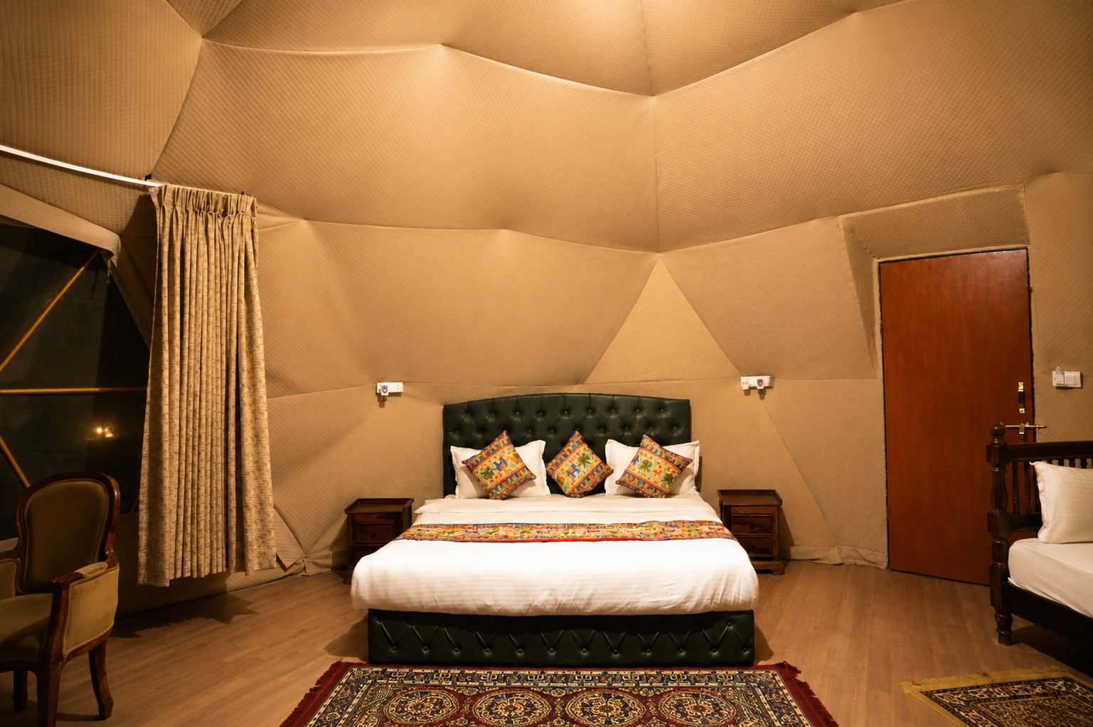 Een slaapkamer met een groot bed, een hoofdbord, twee nachtkastjes, een stoel en een houten deur.