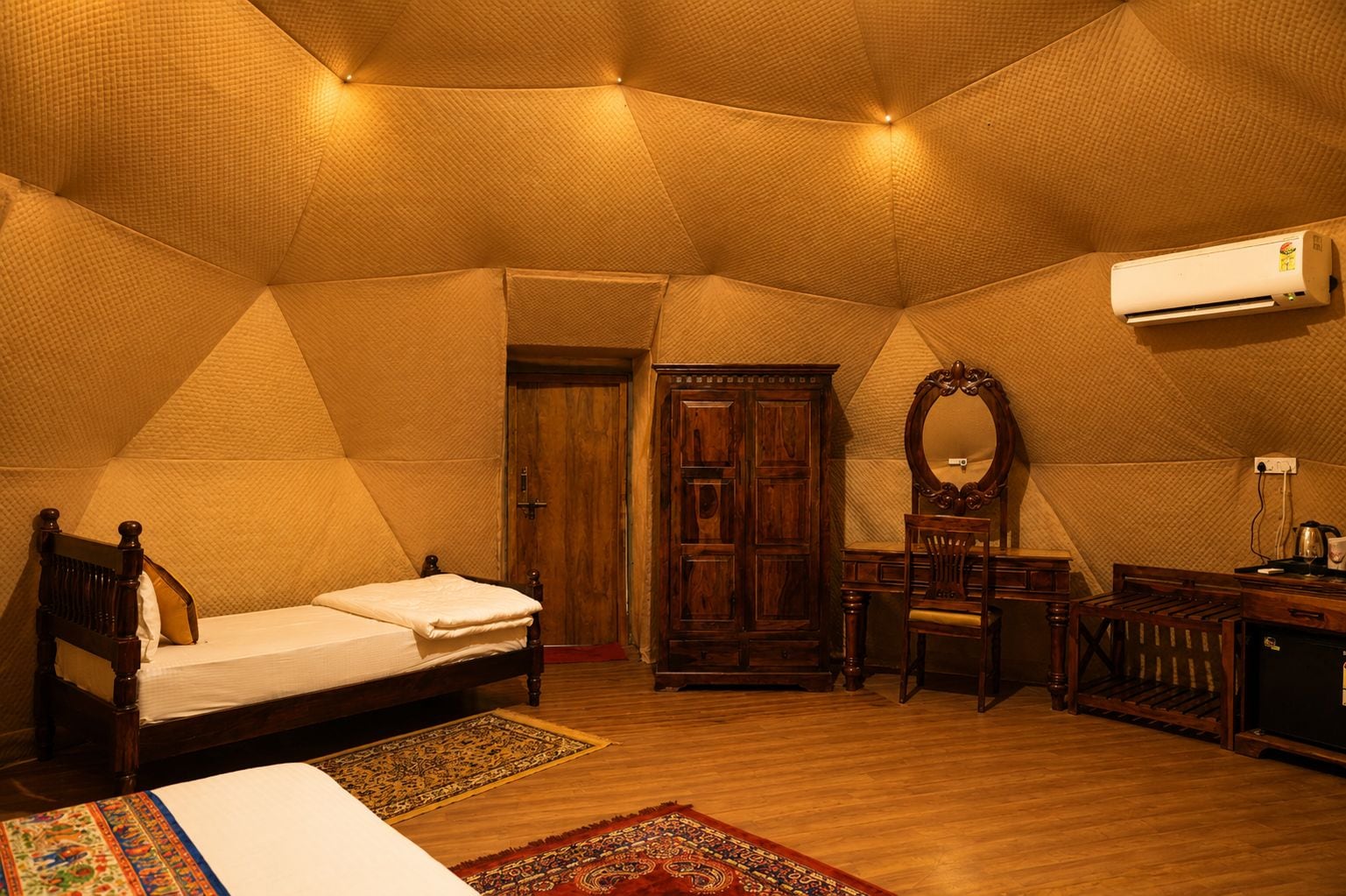 A room with a bed, a wooden wardrobe, a chair, a desk, and an air conditioning unit.