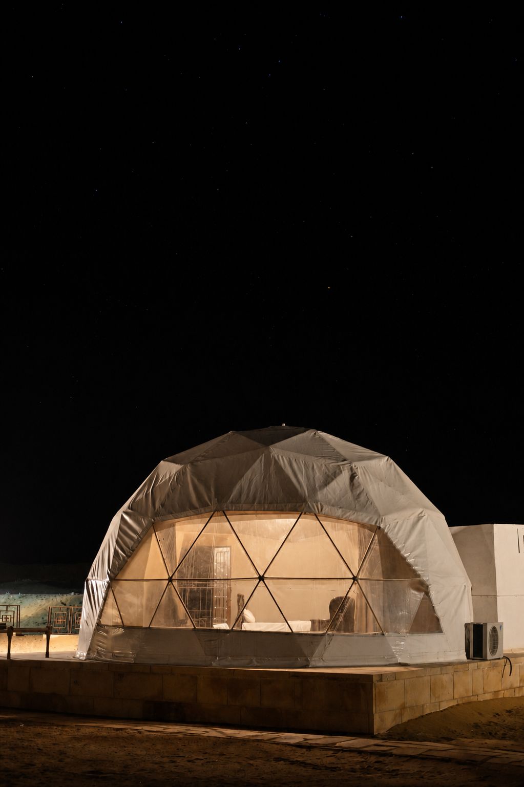 Une structure en forme de dôme, semblable à une tente, dotée d’un intérieur lumineux, qui pourrait servir d’abri temporaire ou d’espace événementiel, se dressant sur fond de ciel nocturne sombre.