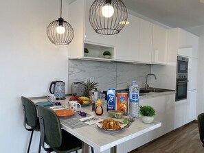 Eine moderne Küche mit weißen Schränken, einer Marmorarbeitsplatte und einem Essbereich mit Stühlen und einem für das Frühstück gedeckten Tisch.
