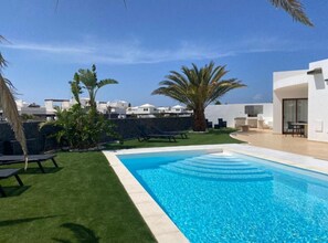 A swimming pool with a clear blue water, surrounded by a well-maintained lawn and palm trees. - Casa Aday, Playa Blanca (Playa Blanca)