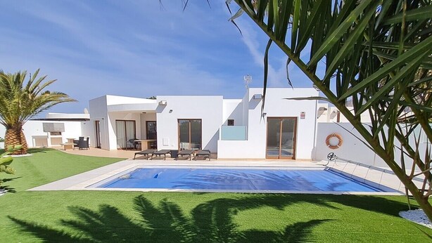 A modern house with a swimming pool, a patio with chairs, and a palm tree. - Casa Aday, Playa Blanca (Playa Blanca)