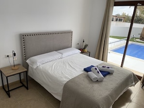 A bedroom with a bed, a bedside table, a lamp, and a view of a swimming pool. - Casa Aday, Playa Blanca (Playa Blanca)