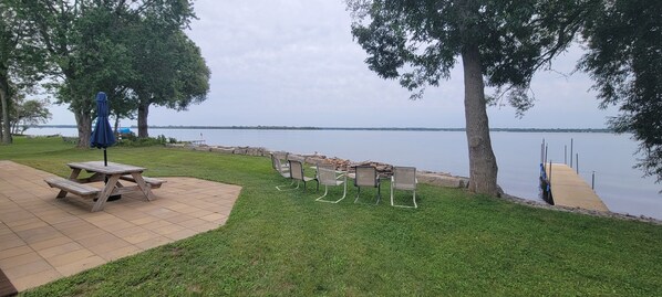 Un área de estar al aire libre con una mesa de picnic y sillas, una sombrilla y vistas a un lago tranquilo.