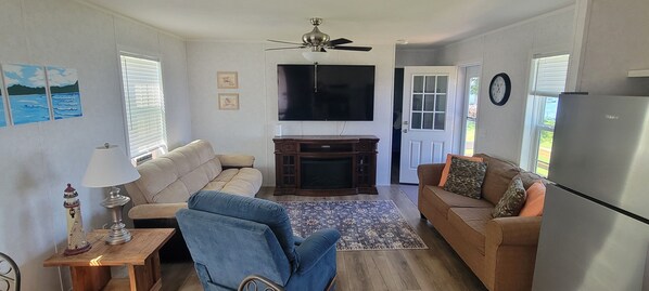 Un salon avec un canapé, un fauteuil, un téléviseur et un ventilateur de plafond.