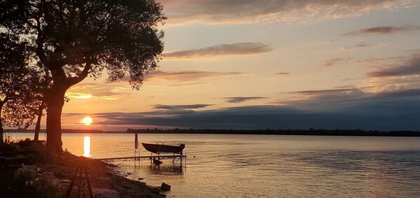 A sunset over a calm lake with a dock and a boat. - New Lakefront Gem- 140ft Private Shoreline & Dock, AC, Kayaks, Firepit (Three Mile Bay)