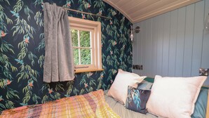 Un dormitorio con cama, ventana y pared decorada con un diseño de hojas.