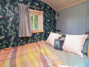 A bedroom with a bed, a window, and a wall with a leaf pattern. - Kingfisher Hut (Sheffield)