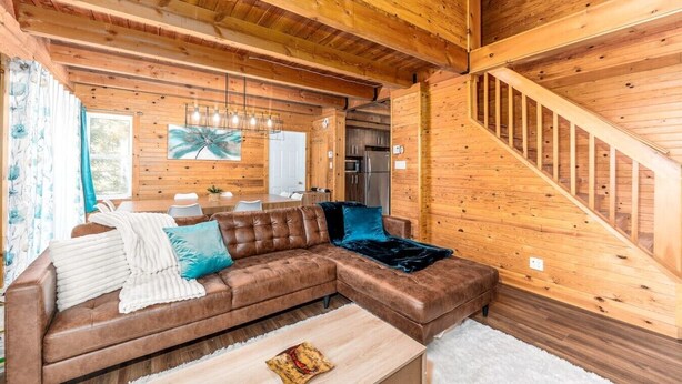A wooden interior with a sofa, a dining table, and a staircase.