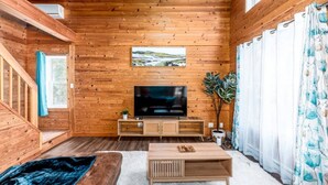 A wooden-paneled room with a TV, a plant, and a sofa.
