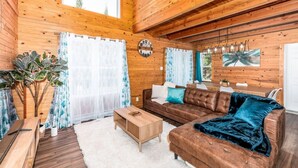 A wooden interior with a sofa, curtains, a clock, and a dining area.
