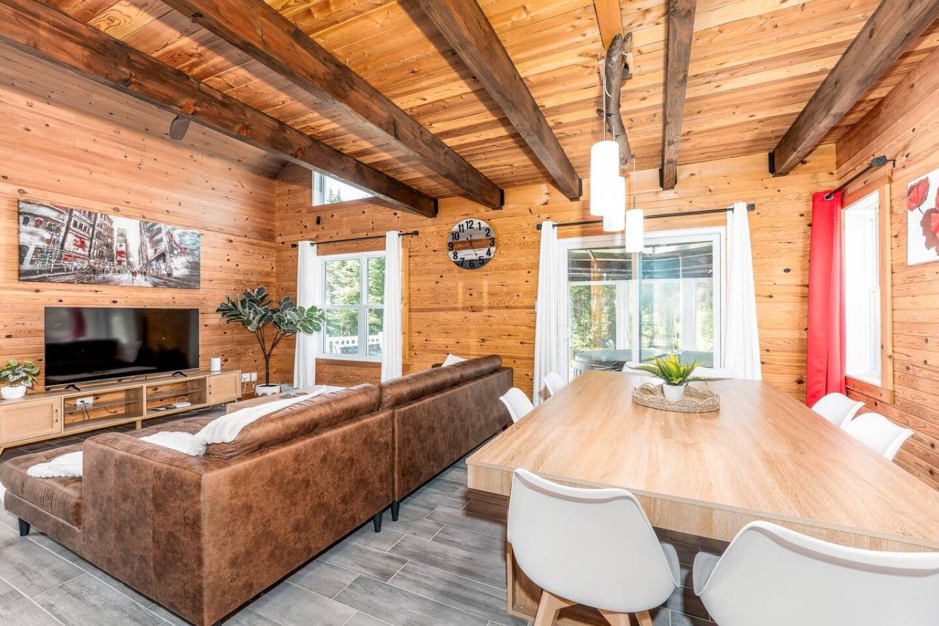 A wooden interior with a TV, sofa, dining table, chairs, and a clock.