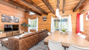 A wooden interior with a TV, sofa, dining table, chairs, and a clock.