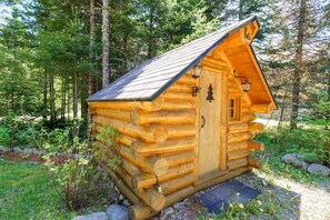 Una cabaña de troncos con puerta y ventanas, rodeada de un bosque.