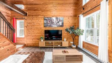 Una sala de estar acogedora con interiores de madera, un televisor de pantalla plana, un sofá cómodo y un ventanal amplio.