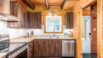 A wooden cabin kitchen with a stove, sink, and dishwasher.