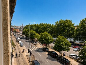 A street view with cars parked along the side, pedestrians walking on the sidewalk, and trees lining the road. - Porto Ribeira Hotel - Studio (Porto)