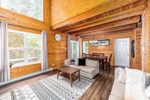 Ein Holzblockbau-Innenraum mit einer Couch, einem Esstisch, Stühlen, einer Uhr und einem großen Fenster.