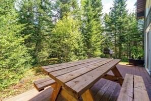 A wooden picnic table on a deck with a view of dense trees.