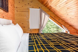 Ein Schlafzimmer mit Bett, einem Fenster mit Vorhängen und Blick auf Bäume.