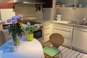Une cuisine avec des meubles blancs, une cuisinière et un évier. On y trouve une table avec un vase de fleurs et un coussin vert.