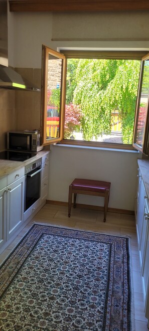 Una cocina con ventana, microondas, horno, banco y alfombra estampada.
