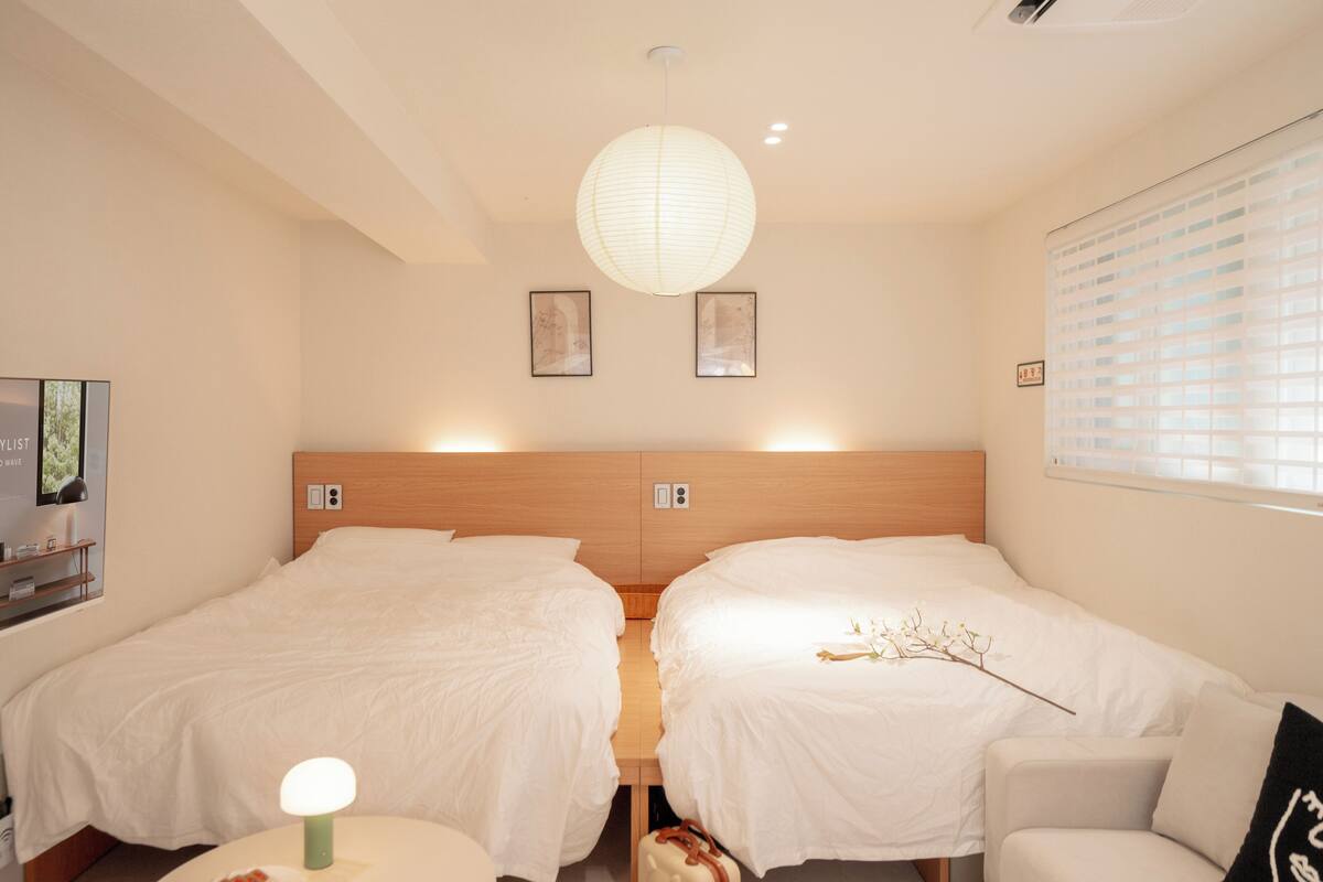 Habitación de hotel con dos camas, cabecero de madera, televisor montado en la pared y un ventanal con persianas.
