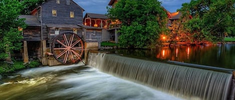 A historic water mill with a large wheel, wooden buildings, and a waterfall.