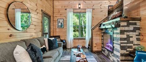 A cozy cabin interior with a wooden interior, a sofa, a table, and a fireplace.