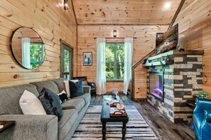 A cozy cabin interior with a wooden interior, a sofa, a table, and a fireplace. - New! 3BR w/Hot Tub*Game Room*Fireplace*Privacy! (Pigeon Forge)