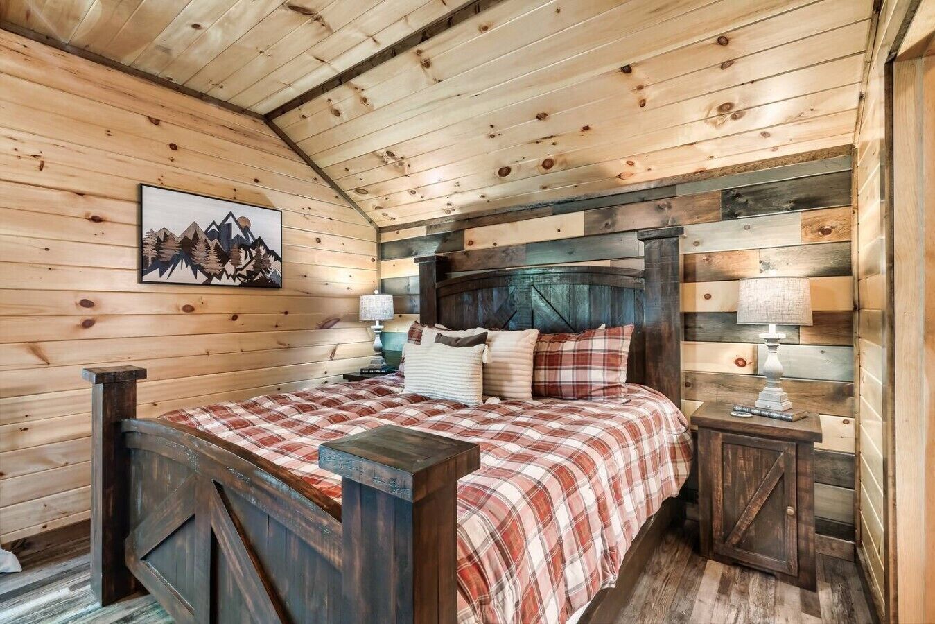 A wooden cabin bedroom with a bed, nightstands, and a mountain painting on the wall.