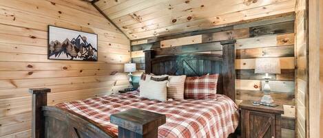 A wooden cabin bedroom with a bed, nightstands, and a mountain painting on the wall.