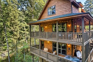 A two-story wooden cabin with a balcony, surrounded by forest. - New! 3BR w/Hot Tub*Game Room*Fireplace*Privacy! (Pigeon Forge)