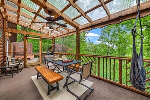 A wooden deck with a table and chairs, a hanging hammock, and a view of the forest. - 2BR w/Treehouse! Hot Tub*Arcade*Fireplace*Privacy! (Sevierville)