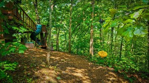 A forested area with a wooden deck and a hanging light fixture. - 2BR w/Treehouse! Hot Tub*Arcade*Fireplace*Privacy! (Sevierville)