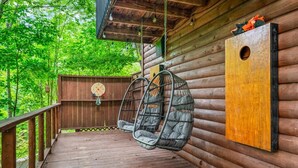 Een houten terras met twee hangstoelen, een houten omheining en een ronde doelschijf aan de muur.
