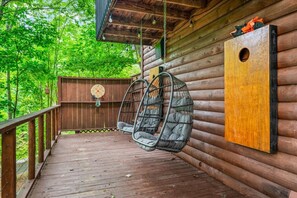 A wooden deck with two hanging chairs, a wooden fence, and a circular target on the wall. - 2BR w/Treehouse! Hot Tub*Arcade*Fireplace*Privacy! (Sevierville)