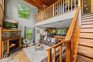 A spacious living area with a fireplace, a sofa, a dining table, and a kitchen in the background. - 2BR w/Treehouse! Hot Tub*Arcade*Fireplace*Privacy! (Sevierville)