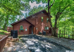 A rustic log cabin with a front door, a small porch, and a gravel driveway. - 2BR w/Treehouse! Hot Tub*Arcade*Fireplace*Privacy! (Sevierville)