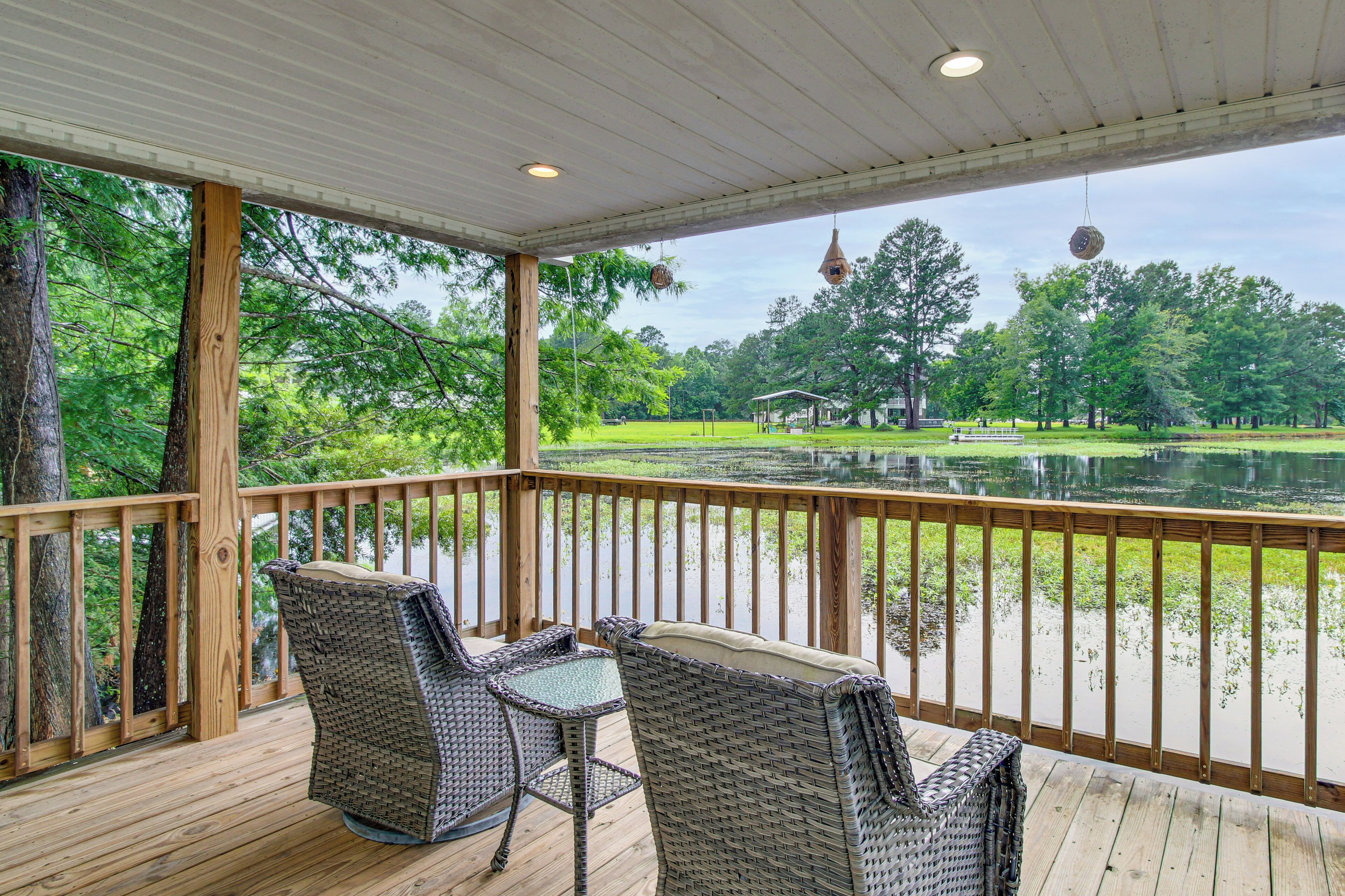 A covered outdoor deck with wicker furniture and a view of a lake and park.