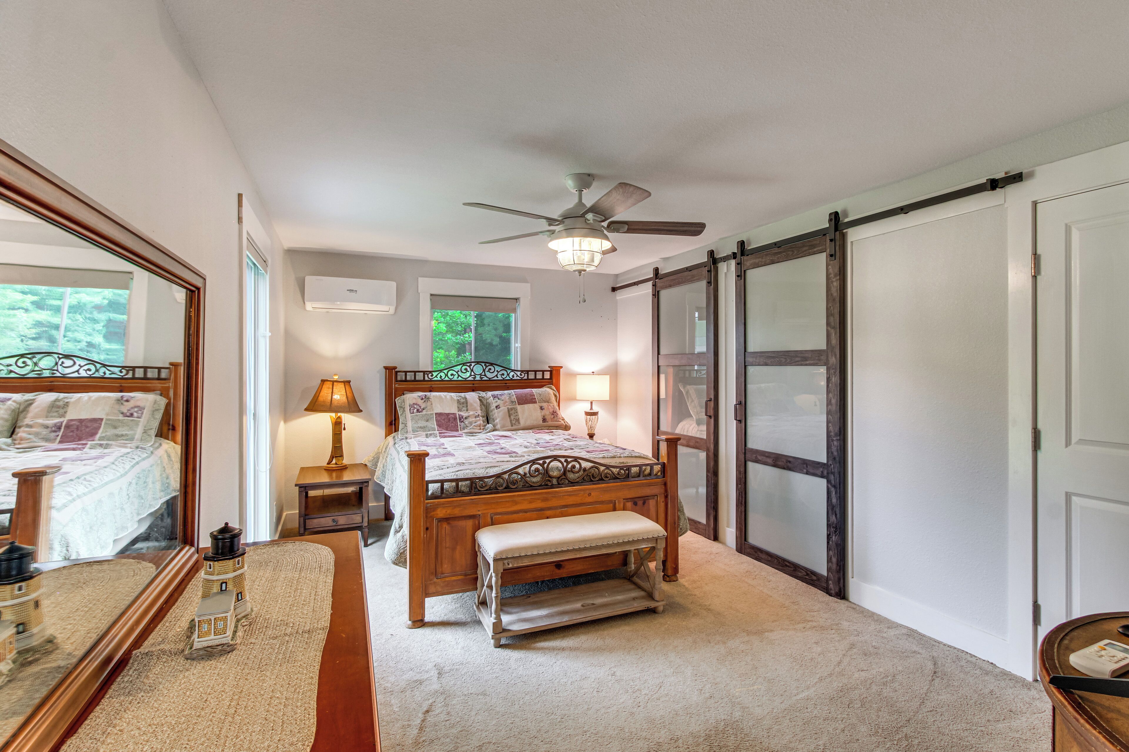 A bedroom with a bed, bench, bedside table, lamp, ceiling fan, and a large mirror.