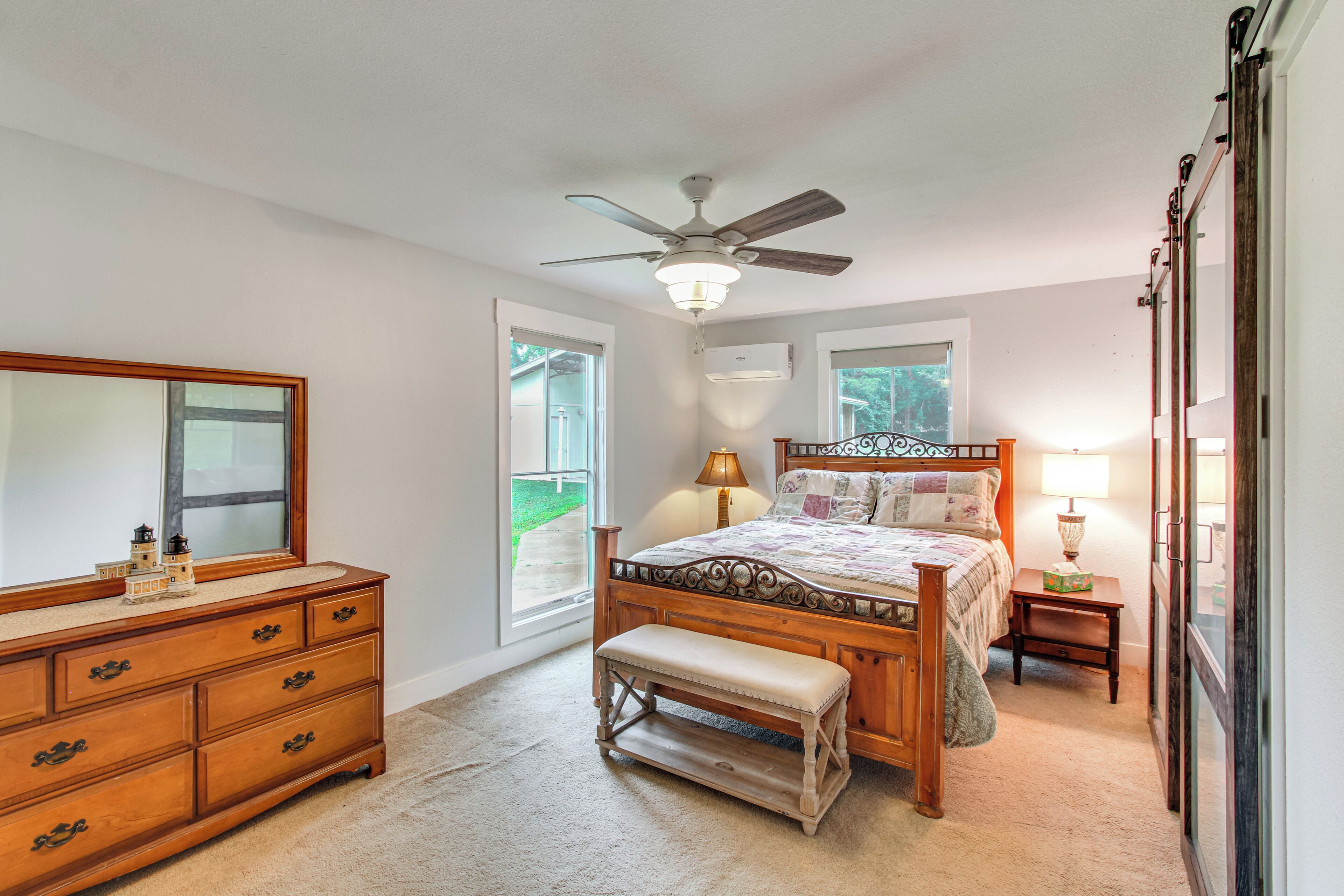 A bedroom with a bed, a dresser, a bench, a ceiling fan, and a window.