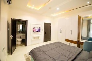 A bedroom with a bed, wardrobe, TV, and a bathroom visible through an open door. - Mind Your Business Villa (Masaka)