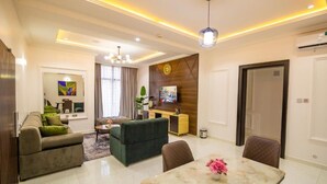 A modern living room with a sofa, a dining table with chairs, a TV, and a decorative wall panel.