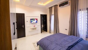 A modern bedroom with a bed, TV, air conditioning unit, and a door leading to another room.