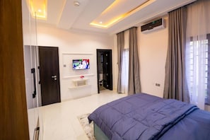 Une chambre moderne équipée d’un lit, d’une télévision, d’un climatiseur et d’une porte donnant sur une autre pièce.