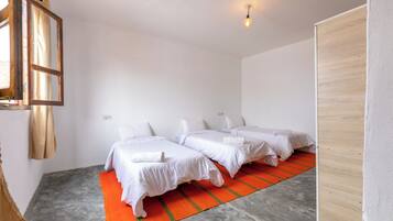 Hotellihuone, jossa on kaksi sänkyä, punavihrearaidallinen matto, puinen vaatekaappi ja riippuvalaisin.