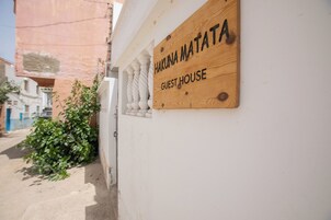 A wooden sign with 'HAKUNA NA'ATA GUEST HOUSE' text, mounted on a white wall with a window above it.